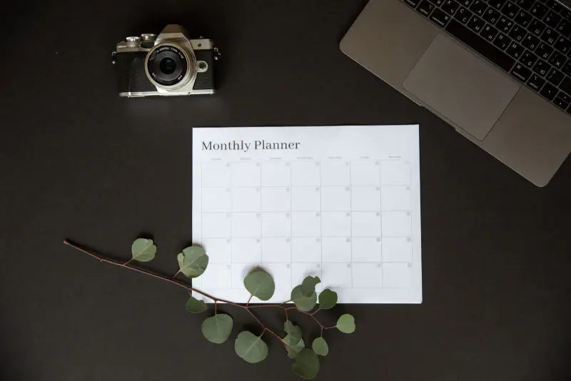 Monthly planner page on a dark desk beside a laptop