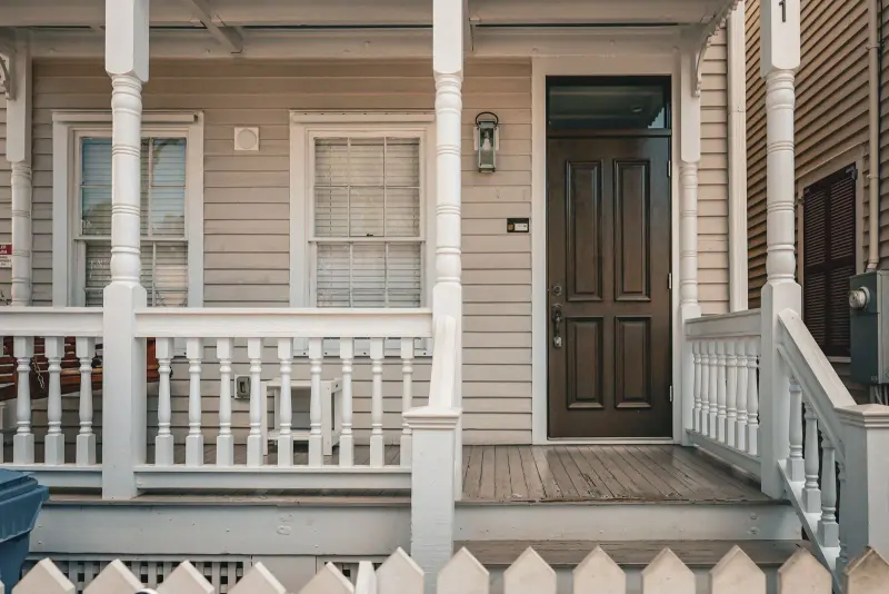 White wooden front porch with a dark front door and picket fence