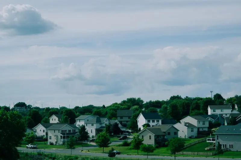 Suburban houses on a green hillside under a cloudy sky