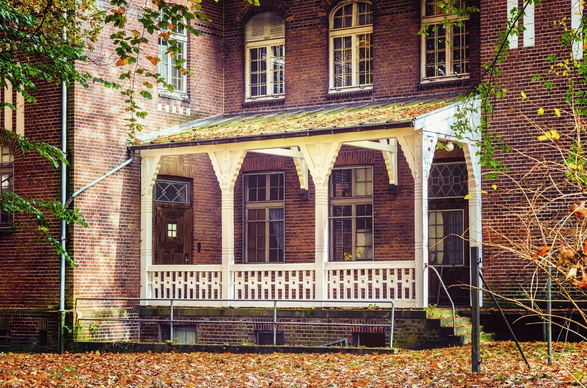 Brick house with a white wooden porch and autumn leaves